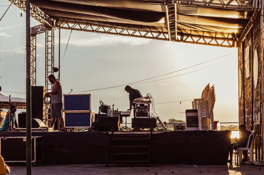 Musicians preparing outdoor stage during sunset with equipment and instruments.